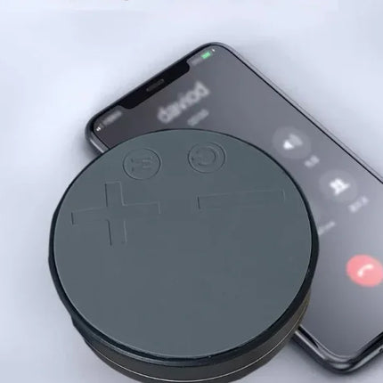 Black circular wireless charger with embossed symbols, charging smartphone on white surface