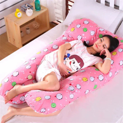 Pink U-shaped pregnancy pillow with cute cartoon faces, supporting pregnant woman in bed for comfort and sleep