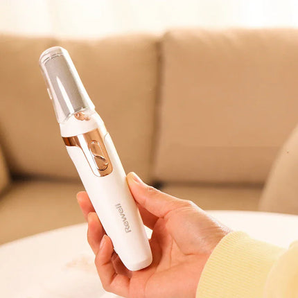 White and gold facial cleansing brush with clear cap, held in hand for skincare routine