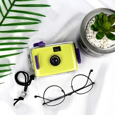 Yellow instant camera with purple accents, minimalist design, paired with glasses and succulent decor