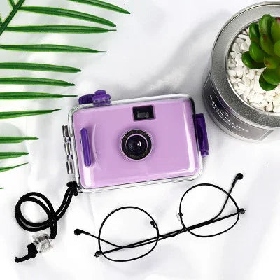 Purple waterproof disposable camera with clear case, black strap, and lens, styled with glasses and succulent