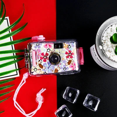 Pink floral disposable camera with strap, set on red and black background with ice cubes and plant